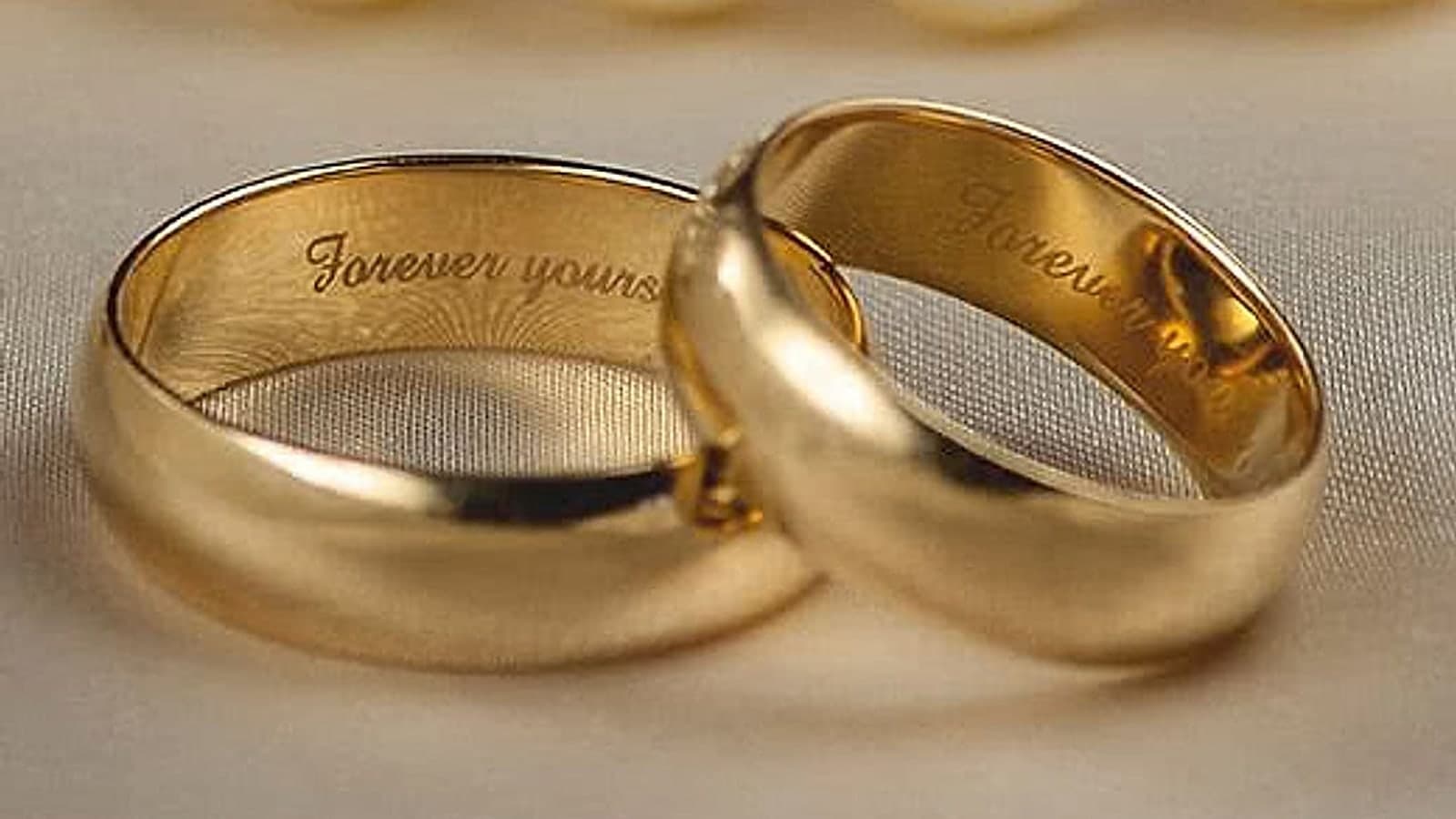 A pair of gold wedding bands resting on cream silk, each engraved inside with the words “Forever yours”.